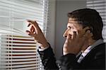 Side view of a young businessman peeking through blinds while on call in the office