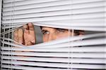 Close-up of a serious young businessman peeking through blinds in the office