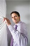 Portrait of a young businessman peeking through blinds in the office