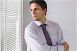 Serious young businessman peeking through blinds in the office