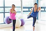 Two fit young women doing the balancing yoga pose in a bright fitness studio