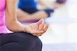 Close-up of cropped sporty women in lotus pose at a bright fitness studio