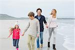 Full length of a happy family of four walking on sand at the beach