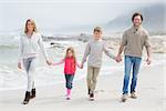 Full length portrait of a happy family of four walking hand in hand at the beach