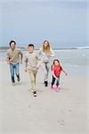 Full length portrait of a happy family of four running at the beach