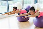 Two fit young women stretching out hands on fitness balls in the bright gym