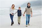 Full length portrait of a happy family of three walking on sand at the beach