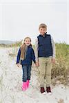 Full length of a happy brother and sister standing hand in hand at the beach