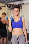 Portrait of a sporty young woman with dumbbell while man using lat machine in the gym