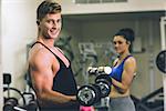 Side view portrait of a young man and woman using dumbbells in the gym