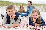 Portrait of happy siblings with parents sitting in background at the beach