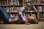 Pretty student lying on library floor reading book in college