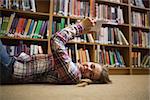 Pretty happy student lying on library floor reading book in college