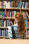 Redhead student reading book from shelf standing in library at the university