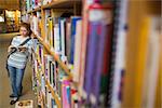 Focused student reading book leaning on shelf in library at the university