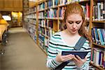 Serious student using tablet standing in library at the university