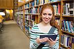 Cheerful student using tablet standing in library at the university