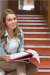 Cheerful young student sitting on stairs looking at camera in college