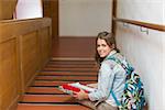 Happy young student sitting on stairs looking up at camera in college