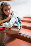 Troubled lonely student sitting on stairs looking at camera in college