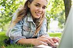 Young smiling student lying on the grass using laptop on college campus