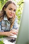 Young smiling student lying on the grass using her laptop on college campus