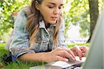 Young focused student lying on the grass using her laptop on college campus