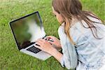 Student lying on the grass using her laptop on college campus