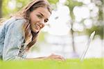 Happy student lying on the grass using her laptop looking at camera on college campus