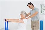 Male therapist assisting senior woman with exercises in the medical office