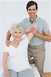 Male physiotherapist stretching a smiling senior woman's arm in the medical office