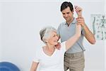 Male physiotherapist stretching a smiling senior woman's arm in the medical office