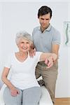 Male physiotherapist stretching a senior woman's arm in the medical office