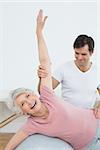 Physical therapist assisting senior woman with yoga ball in the gym at hospital