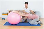 Side view of a physical therapist assisting senior woman with yoga ball in the gym at hospital