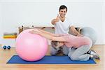 Portrait of a physical therapist gesturing thumbs up by senior woman with yoga ball in the gym at hospital