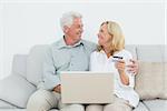 Relaxed senior couple doing online shopping through laptop and credit card on sofa in a house
