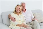 Portrait of a relaxed happy senior couple with remote control sitting on sofa in a house