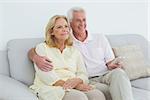 Relaxed happy senior couple with remote control sitting on sofa in a house