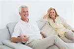 Relaxed cheerful senior couple with remote control sitting on sofa in a house