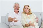 Portrait of a relaxed cheerful senior couple watching television in a house