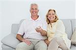 Portrait of a relaxed cheerful senior couple watching television in a house