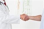 Close-up mid section of a doctor and patient shaking hands in the medical office