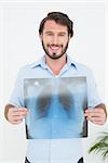 Portrait of a smiling young man holding lung x-ray over white background