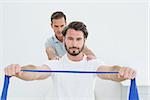 Male therapist assisting young man with exercises in the medical office