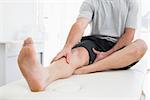 Low section of a young man with his hands on a painful leg while sitting on examination table