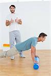 Portrait of physical therapist gesturing thumbs up with young man doing push ups in the gym at hospital