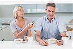 Couple reading text messages while having breakfast in the kitchen at home