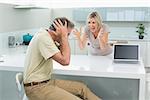 Tired man covering his ears as woman argue in the kitchen at home