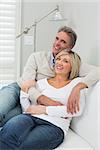 Happy man and woman embracing while sitting on sofa in living room at home